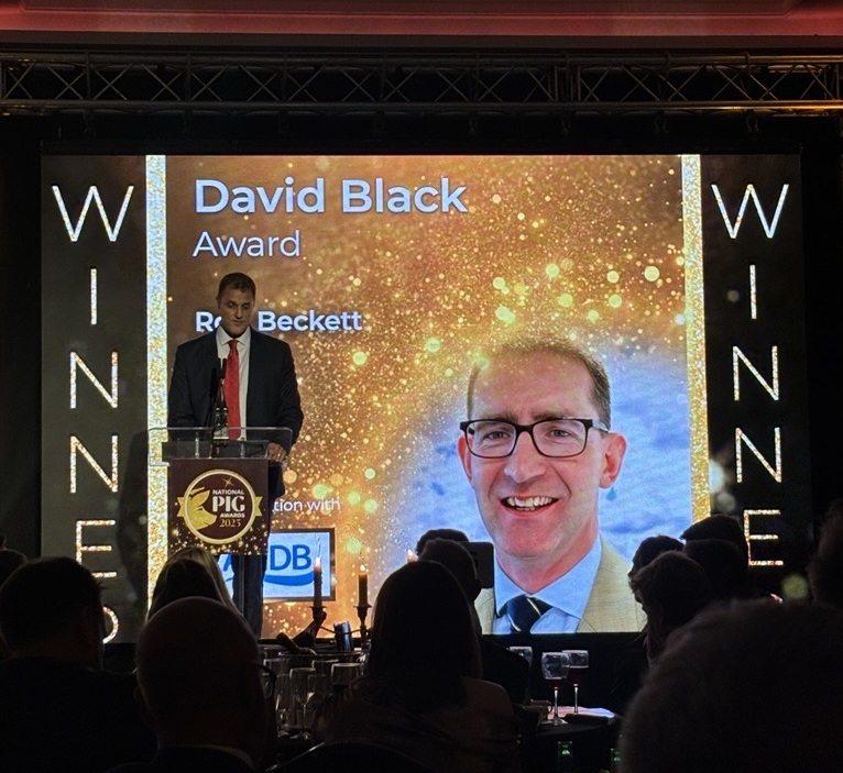 Man stood on stage in front of a screen announcing David Black Award winner.